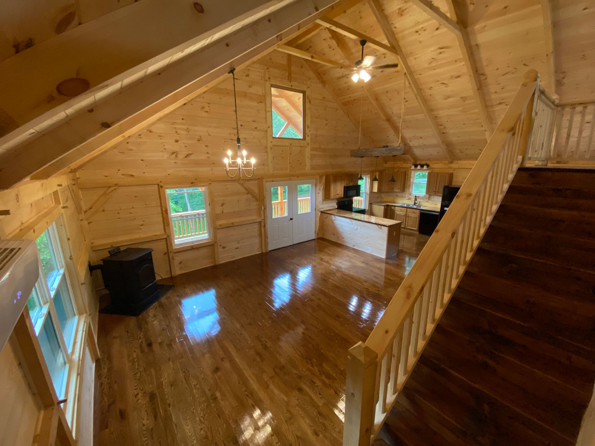 Interior view of a wooden cabin with a staircase, hardwood floors, and a kitchen area.