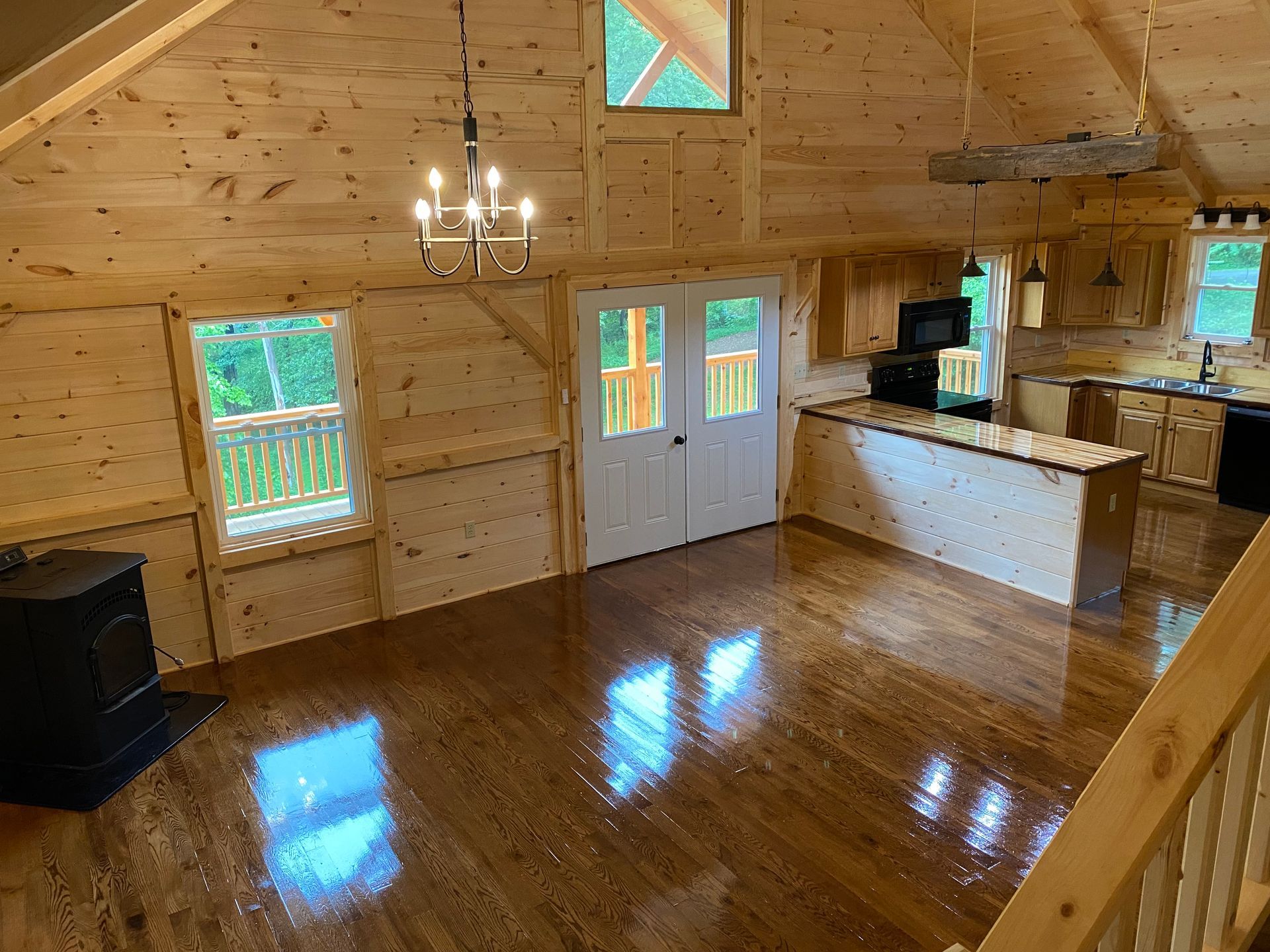 Interior of a cabin with wooden walls, hardwood floors, and a kitchen area.