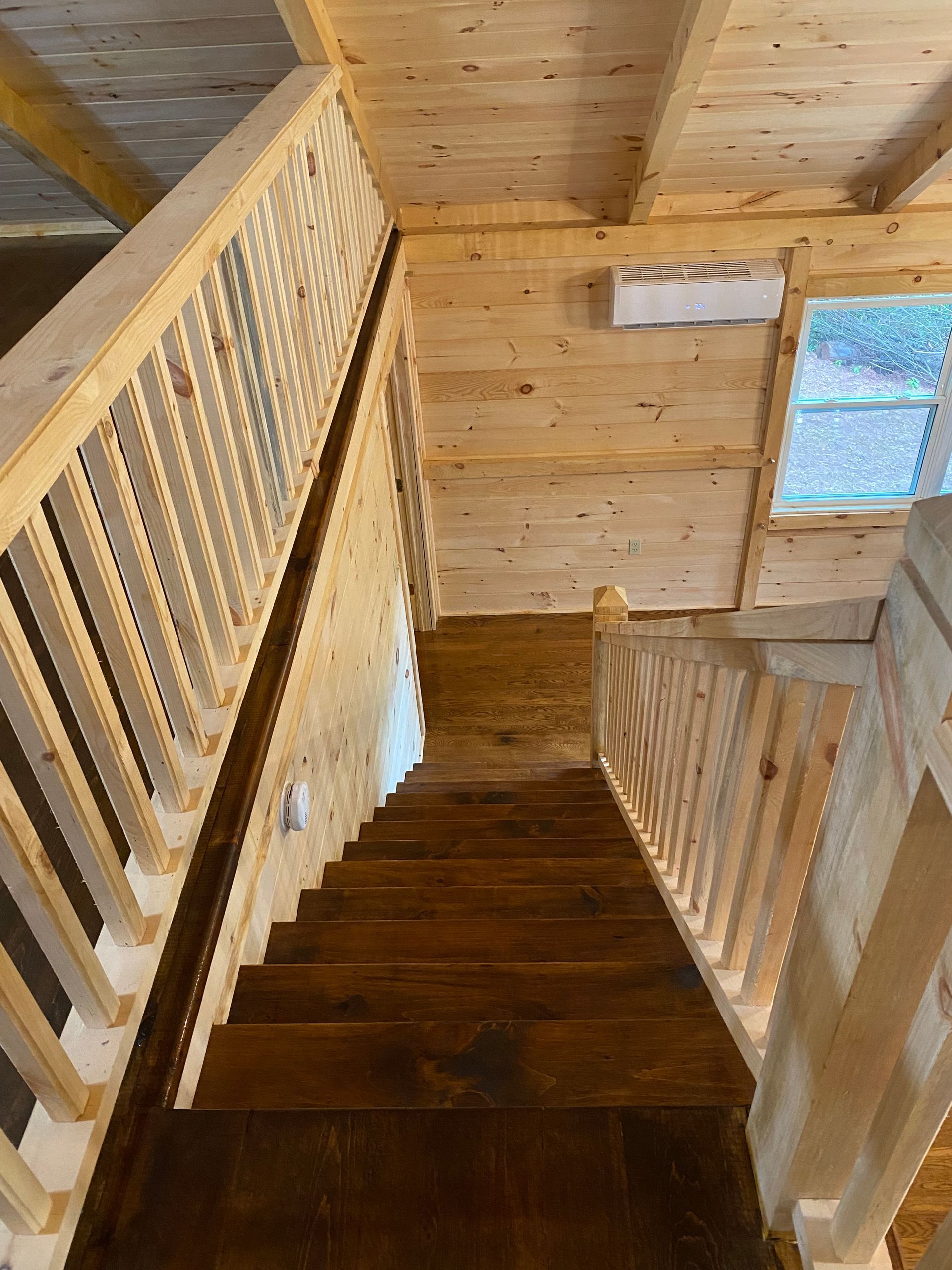 Wooden staircase in a cabin, viewed from above. Dark steps, light railings, and wood walls.