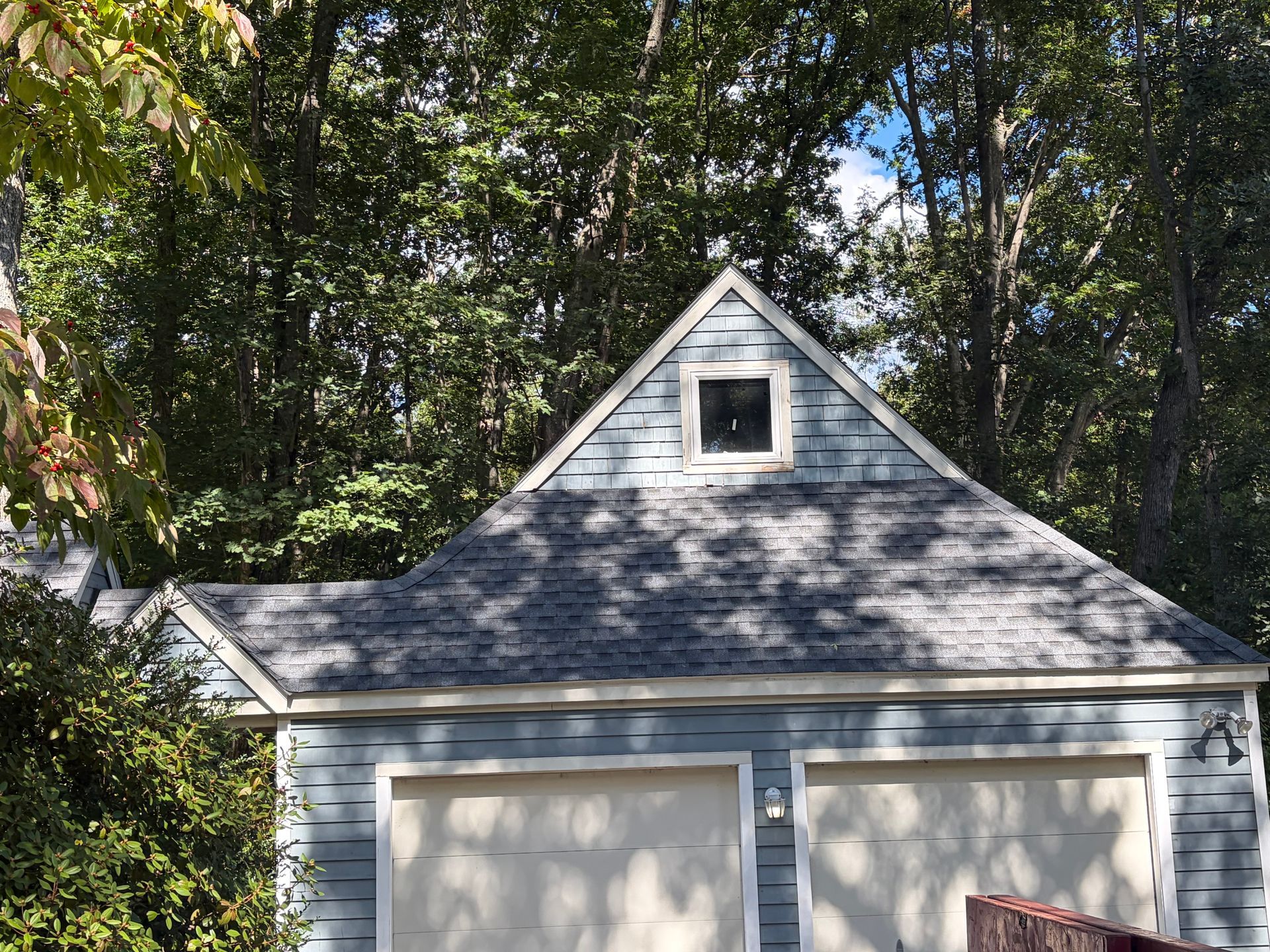 Gray garage with twin doors and a peaked roof under trees in a wooded yard
