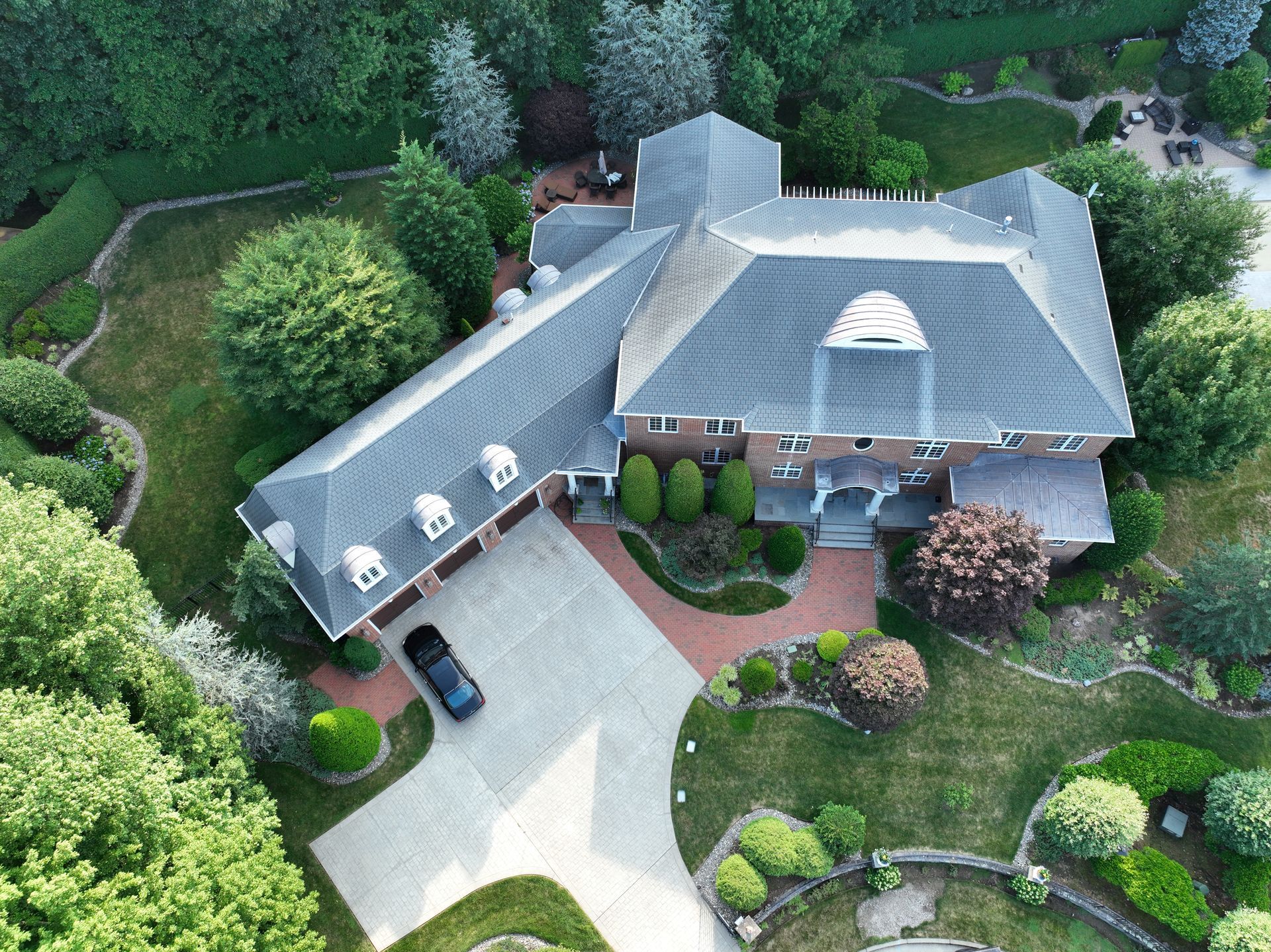 Aerial view of a large gray-roofed house with a curved driveway and lush green landscaping.