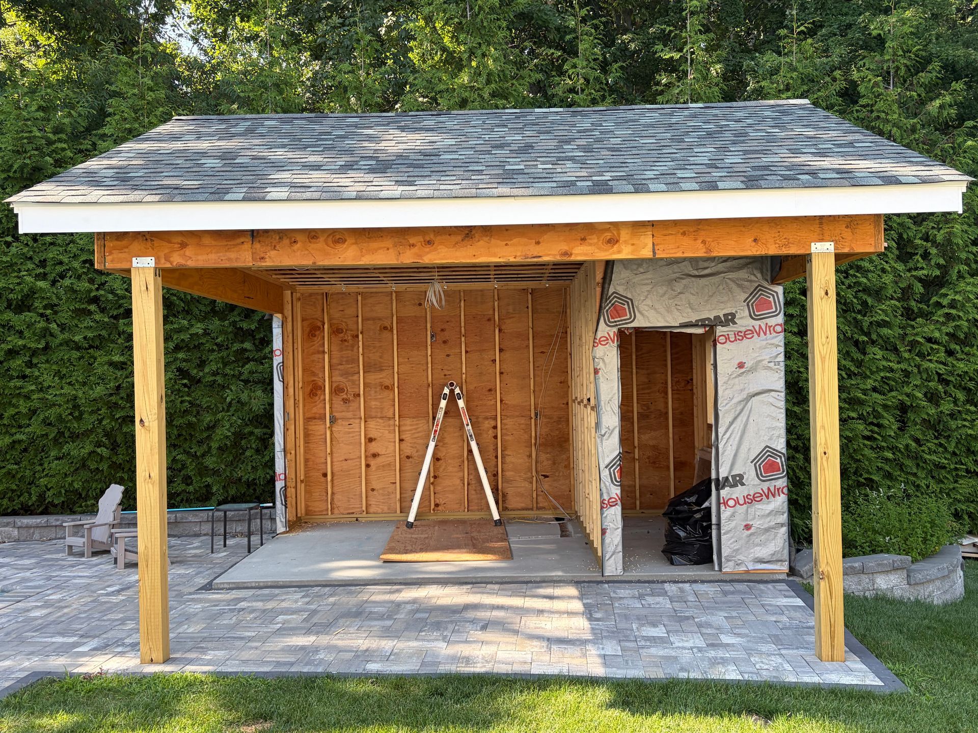 Small unfinished wooden shed with a sloped roof, open front, and a ladder inside on a concrete pad.