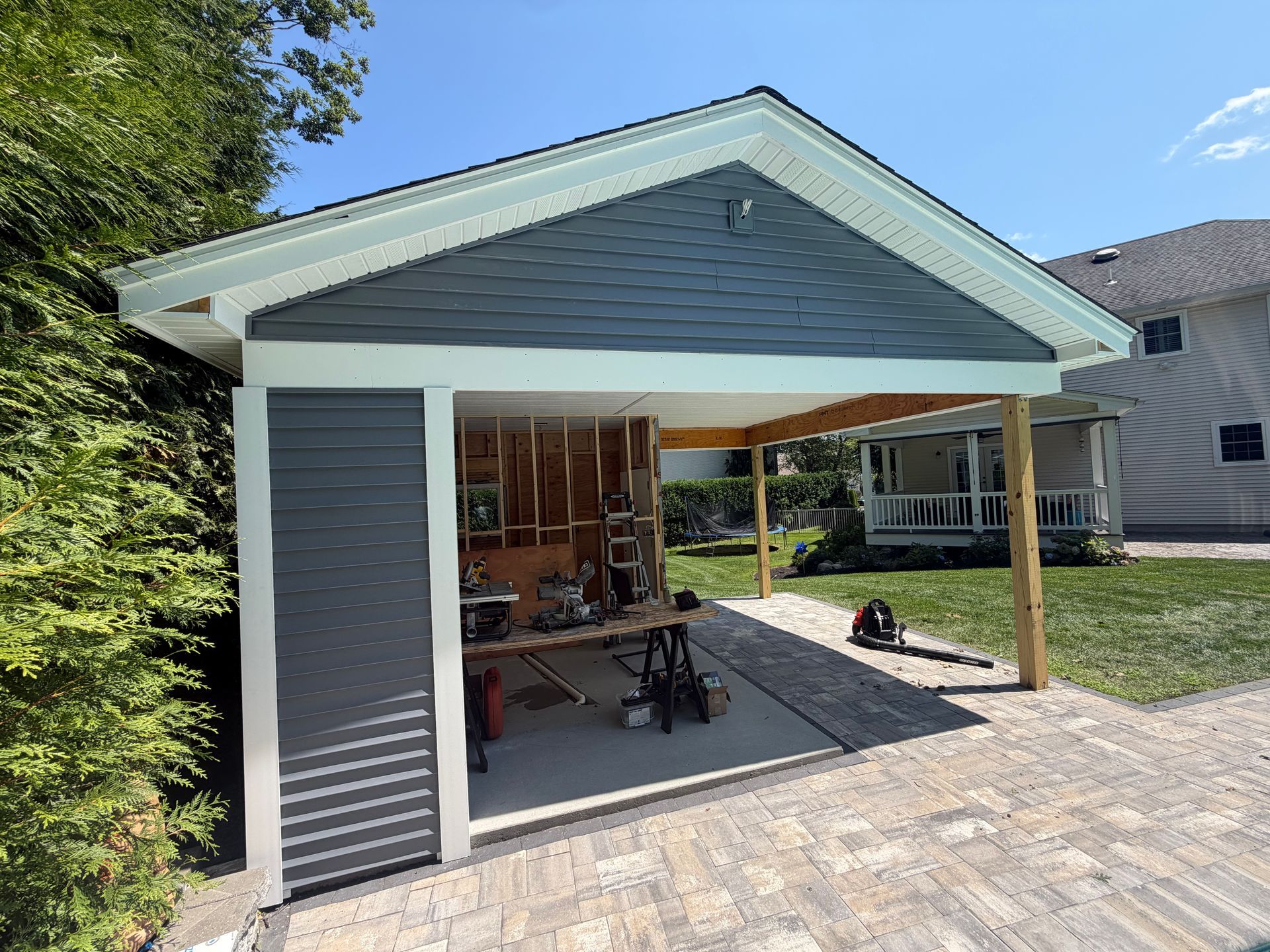 Covered backyard patio with gray siding, wooden posts, and outdoor seating beside a house
