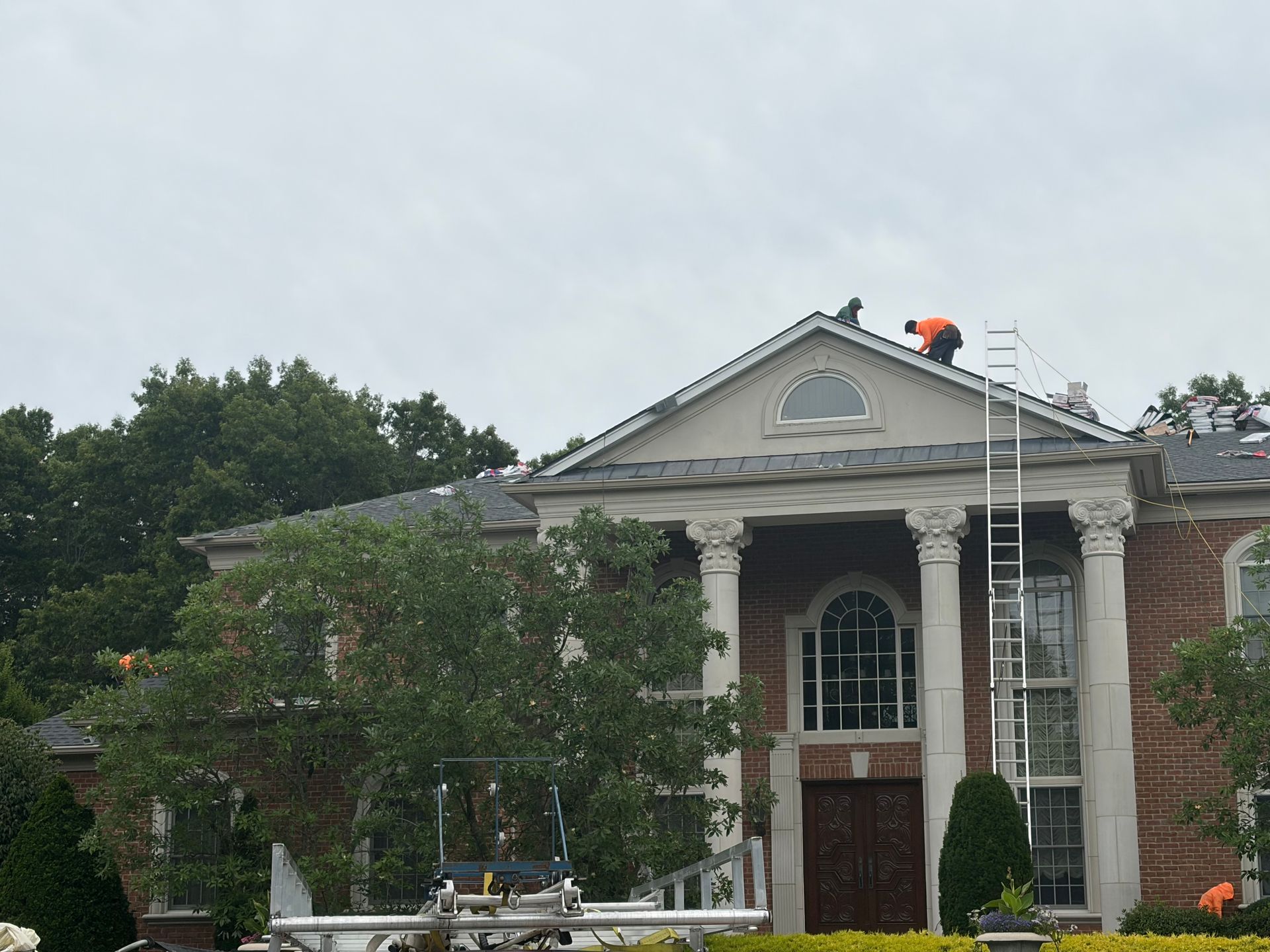 Brick building with white columns and arched windows, a ladder on the roof, and trees in front