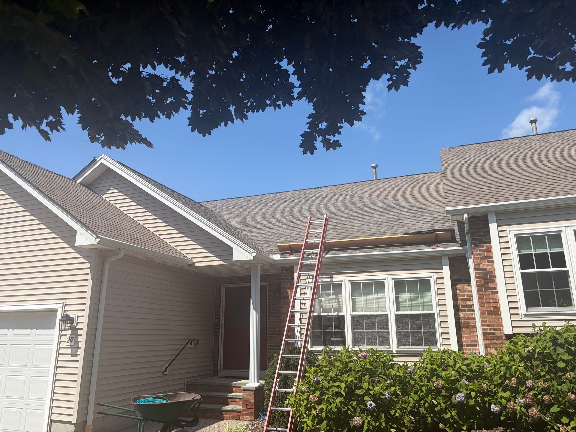 Suburban house exterior with white siding, brick columns, and a red ladder leaning against the roofline.