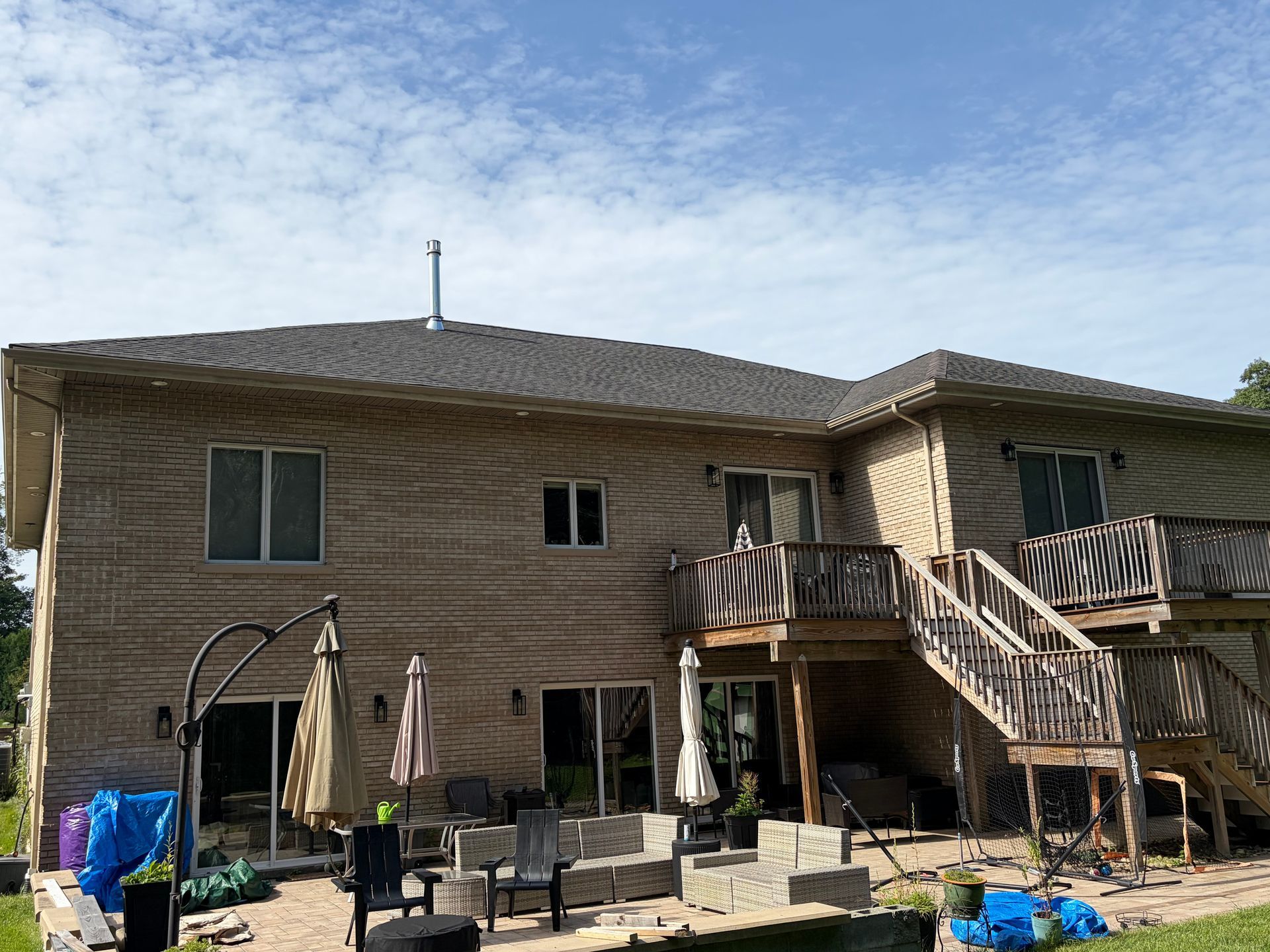 Backyard with a two-story house, wooden deck stairs, and patio furniture under a partly cloudy sky