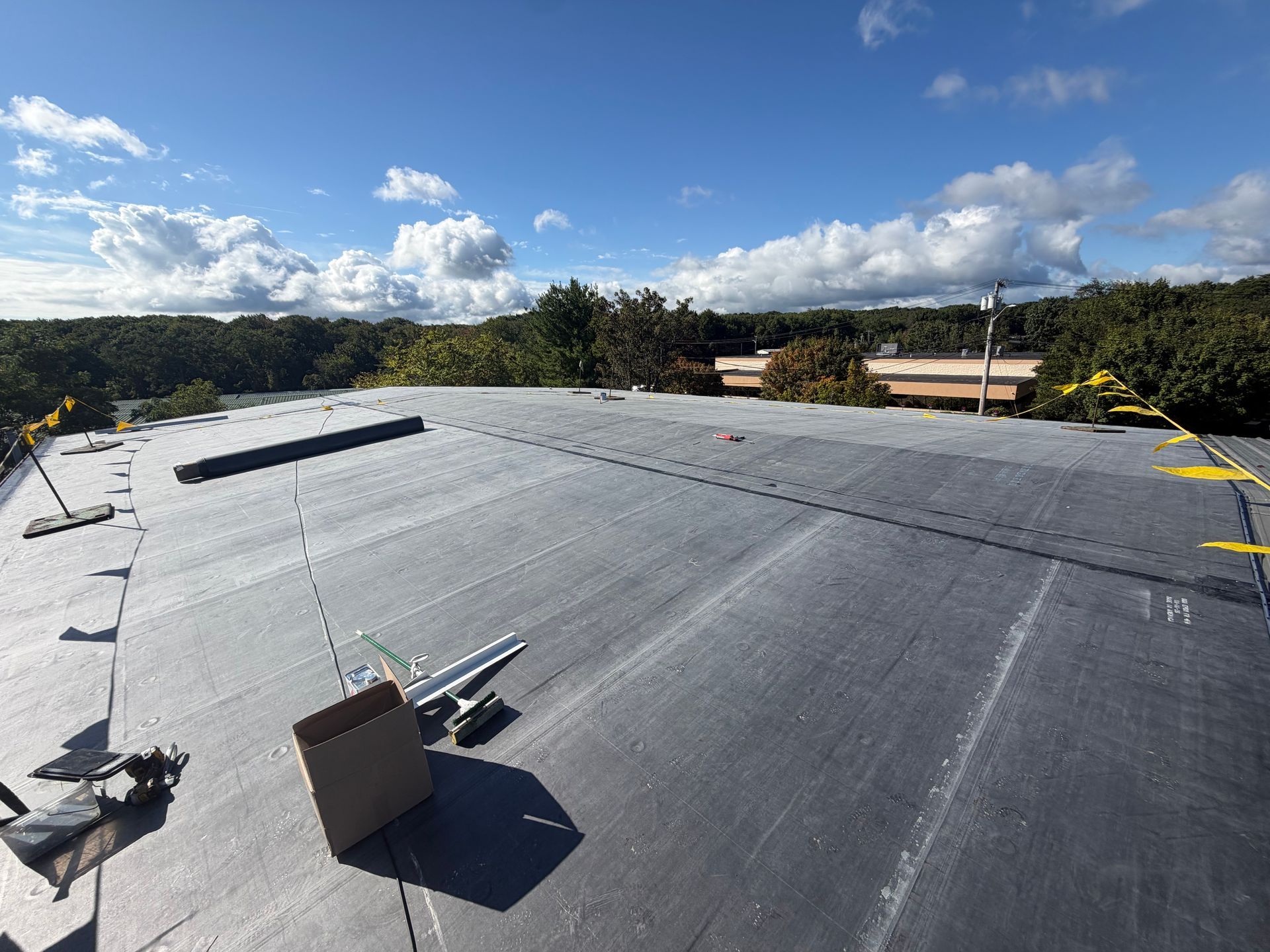 Flat black rooftop with vents and equipment under a partly cloudy sky.
