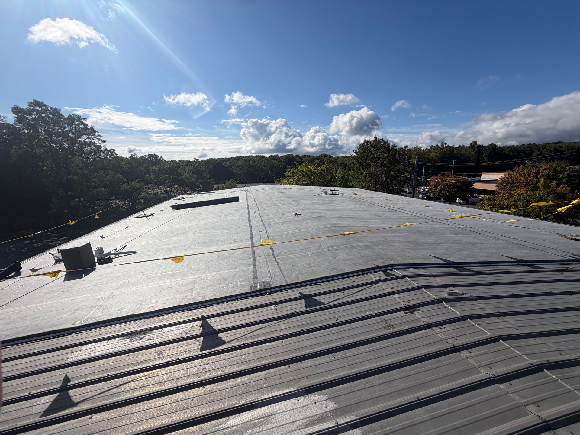 Rooftop under construction with gray underlayment, trees and blue sky in the background