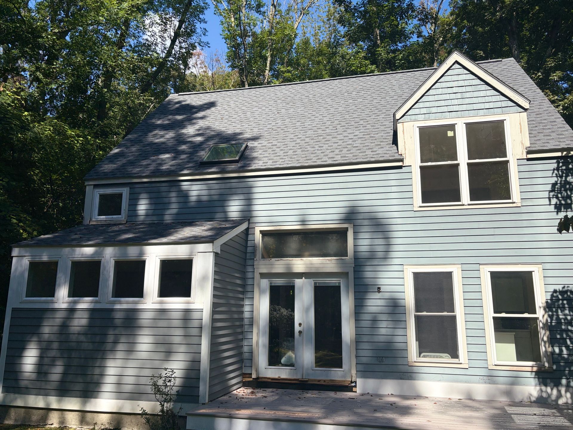 Blue two-story house with gray roof, white trim, and attached garage in a wooded yard