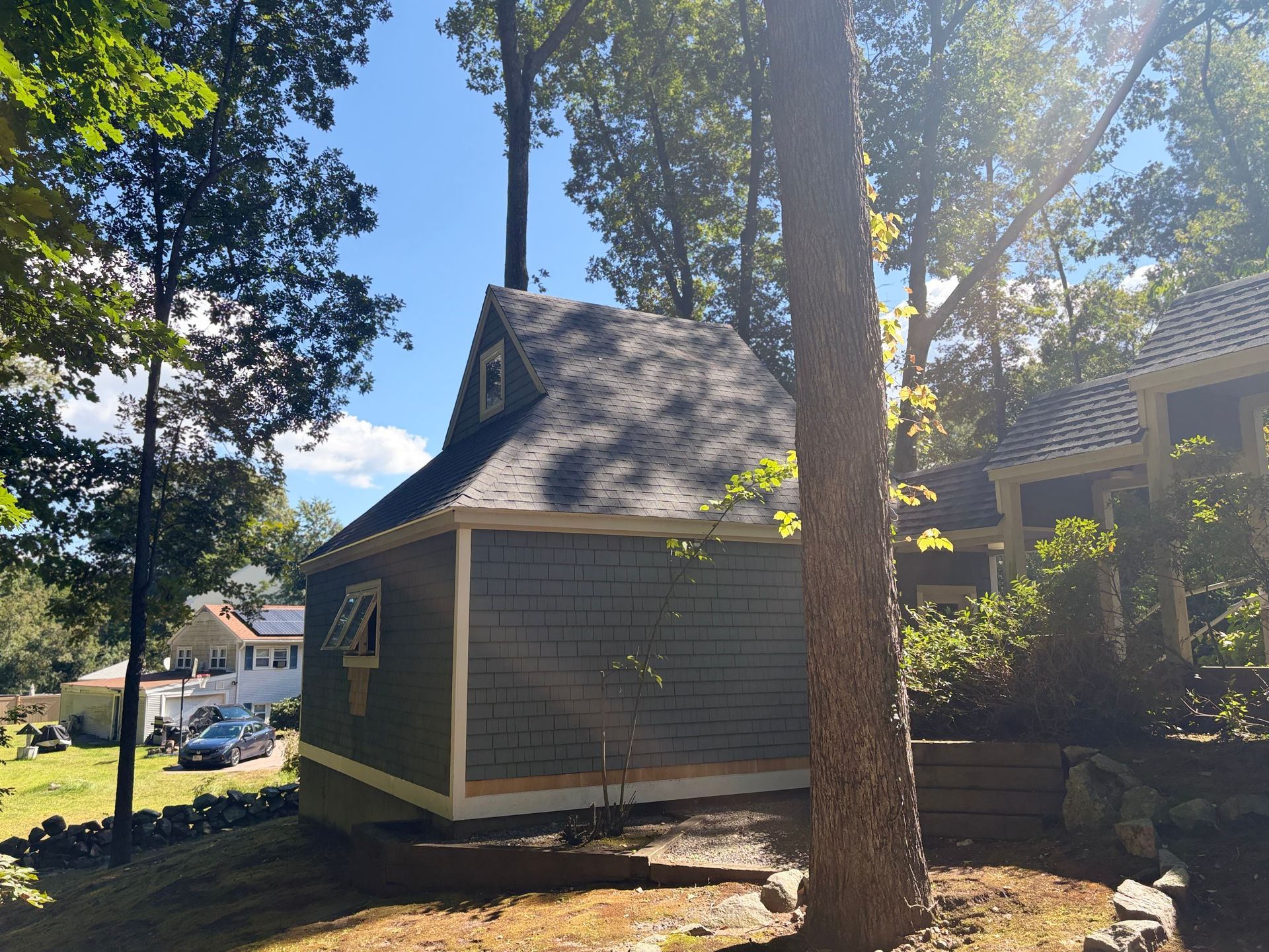 Small green house with steep roof among tall trees in a sunny yard