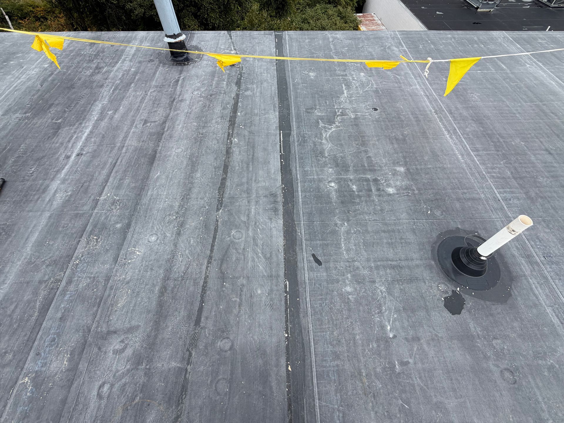 Gray flat roof with a vent pipe, roof seam, and yellow caution flags along the top edge.