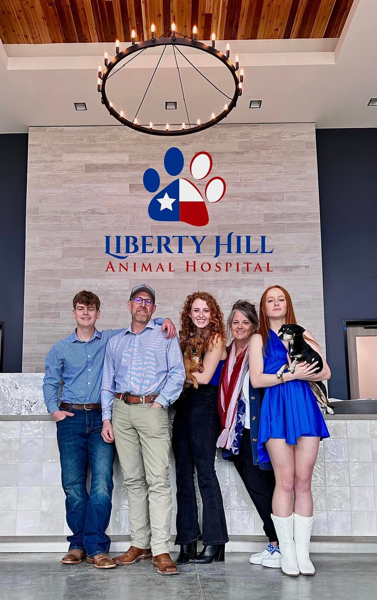 Family poses in front of the Liberty Hill Animal Hospital sign. The sign has a paw print and the Texas flag. People smile.