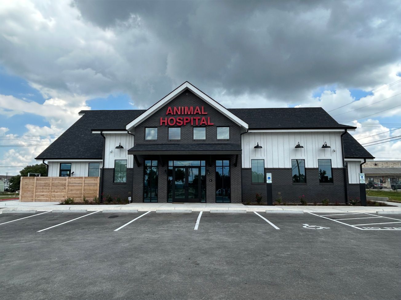 Exterior view of an animal hospital with dark and light siding, red lettering, and a parking lot.