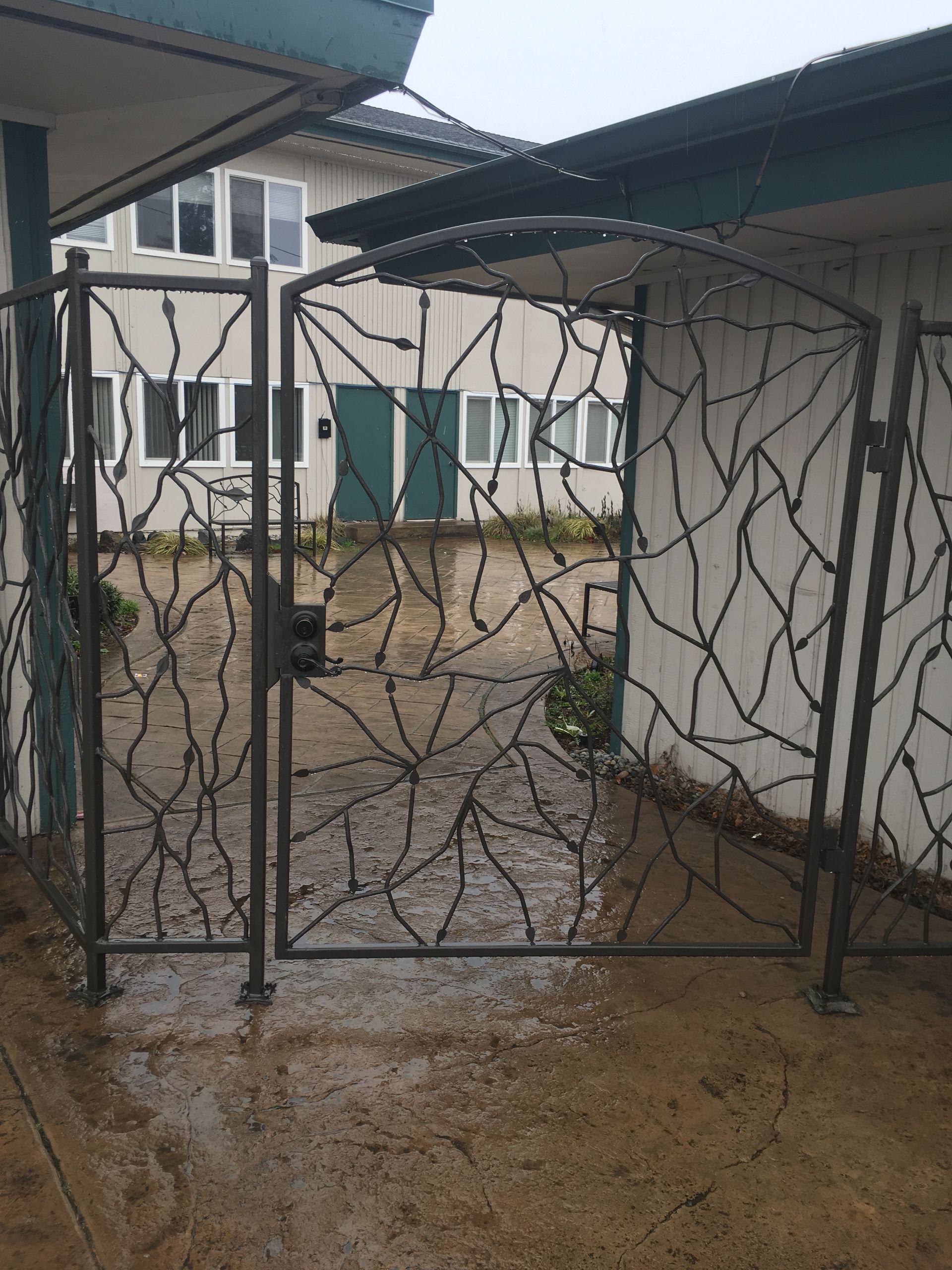 A wrought iron gate with a pattern on it is in front of a building.
