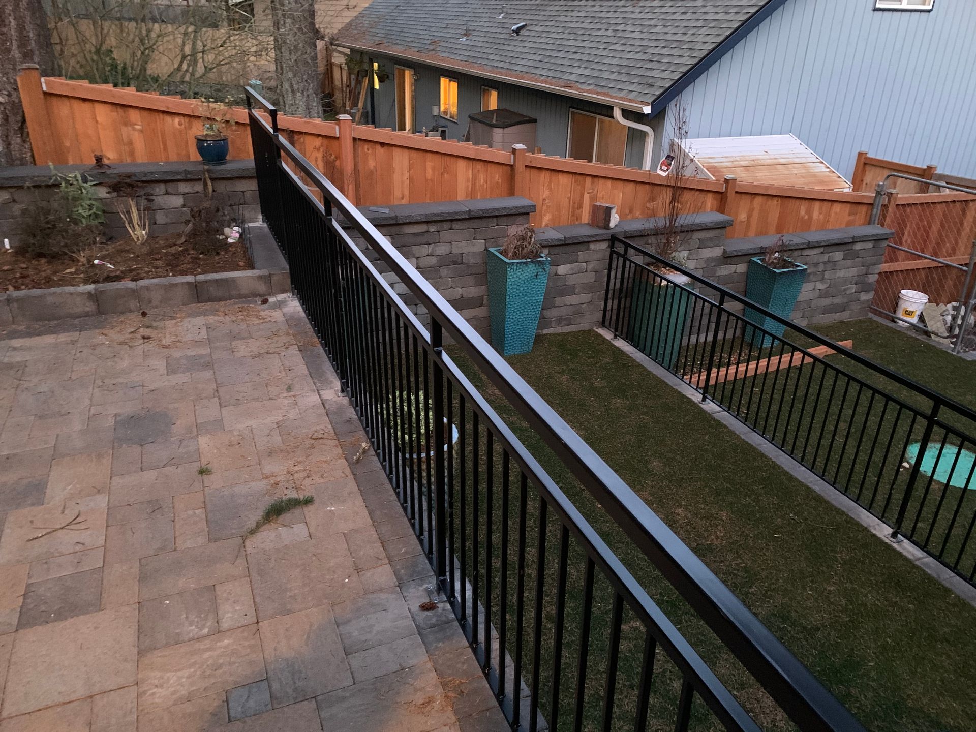 A black railing leading to a patio with a wooden fence in the background
