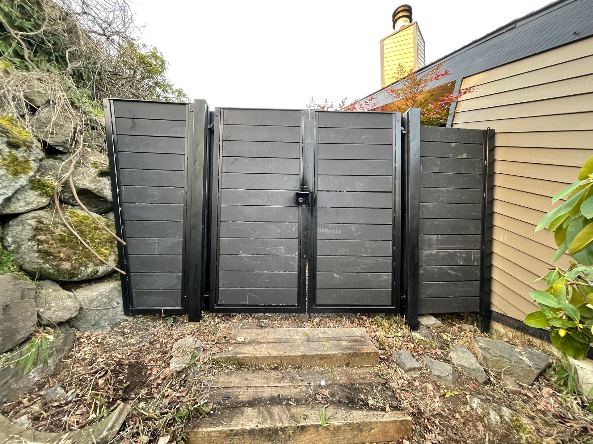 A black gate with stairs leading to it is in front of a house