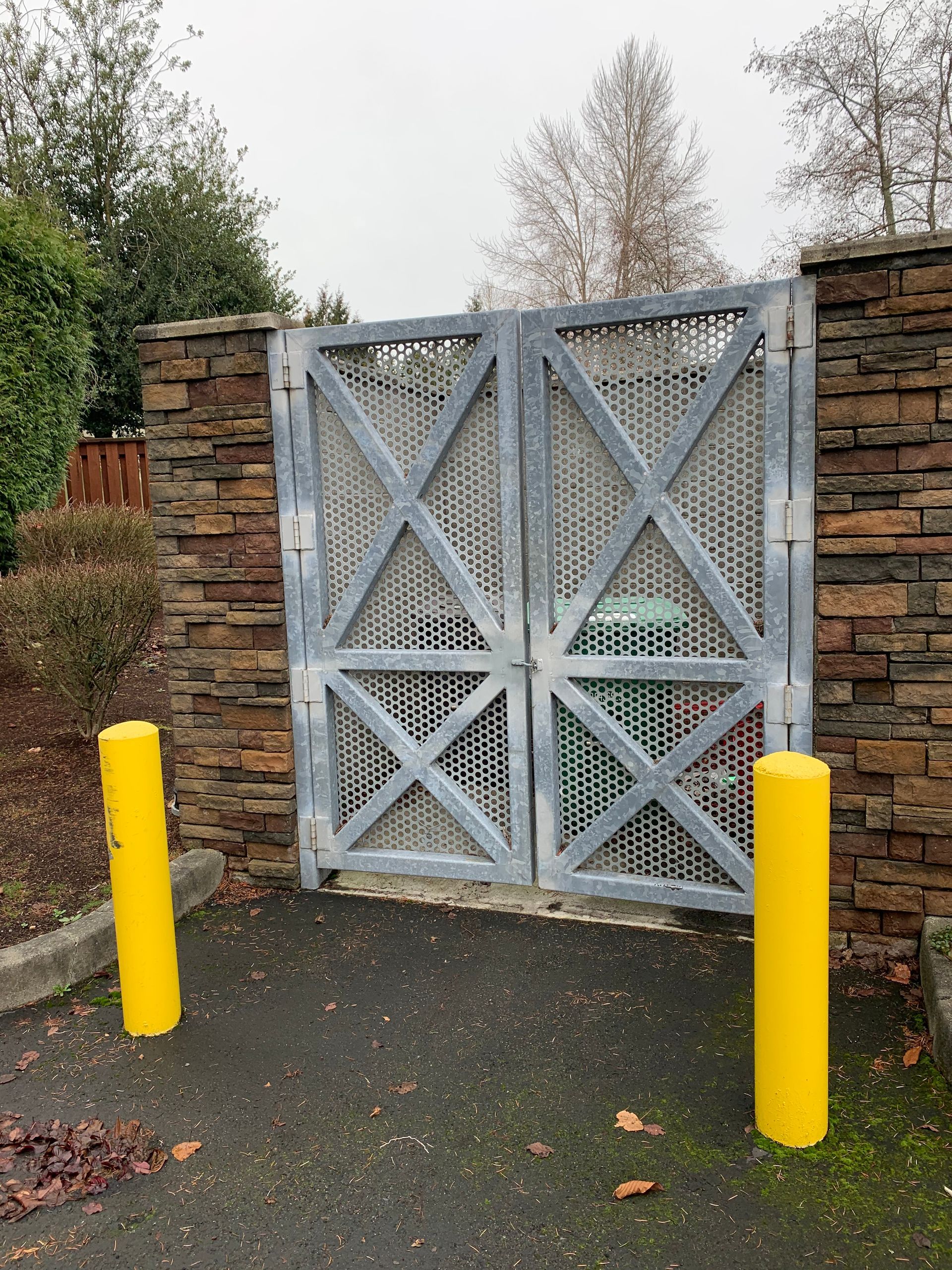 A metal gate is surrounded by yellow poles and a stone wall