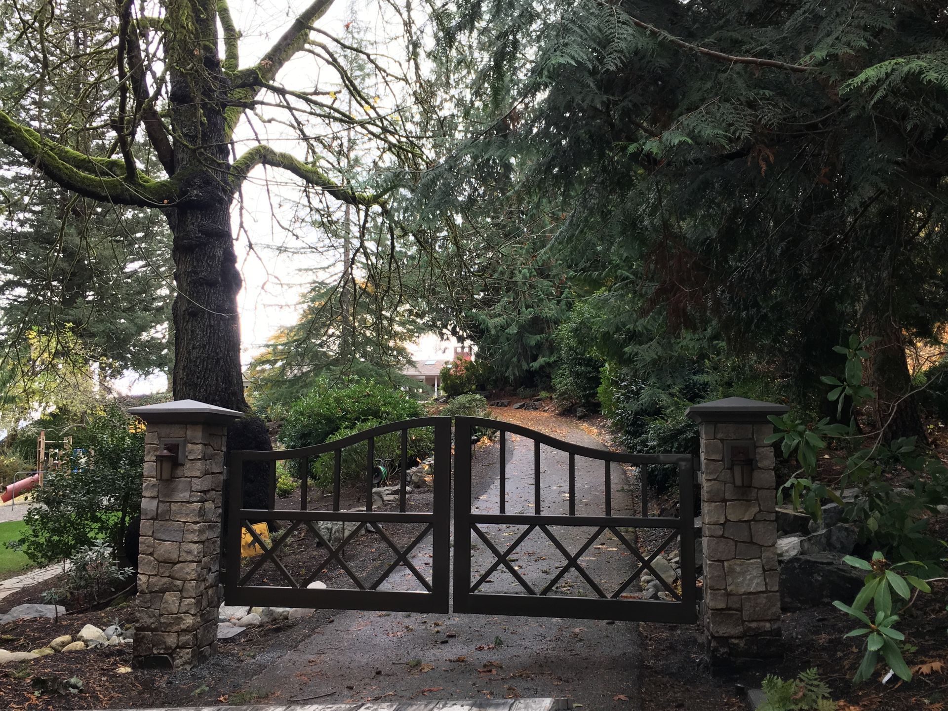 A concrete driveway with a stone pillar and a metal gate