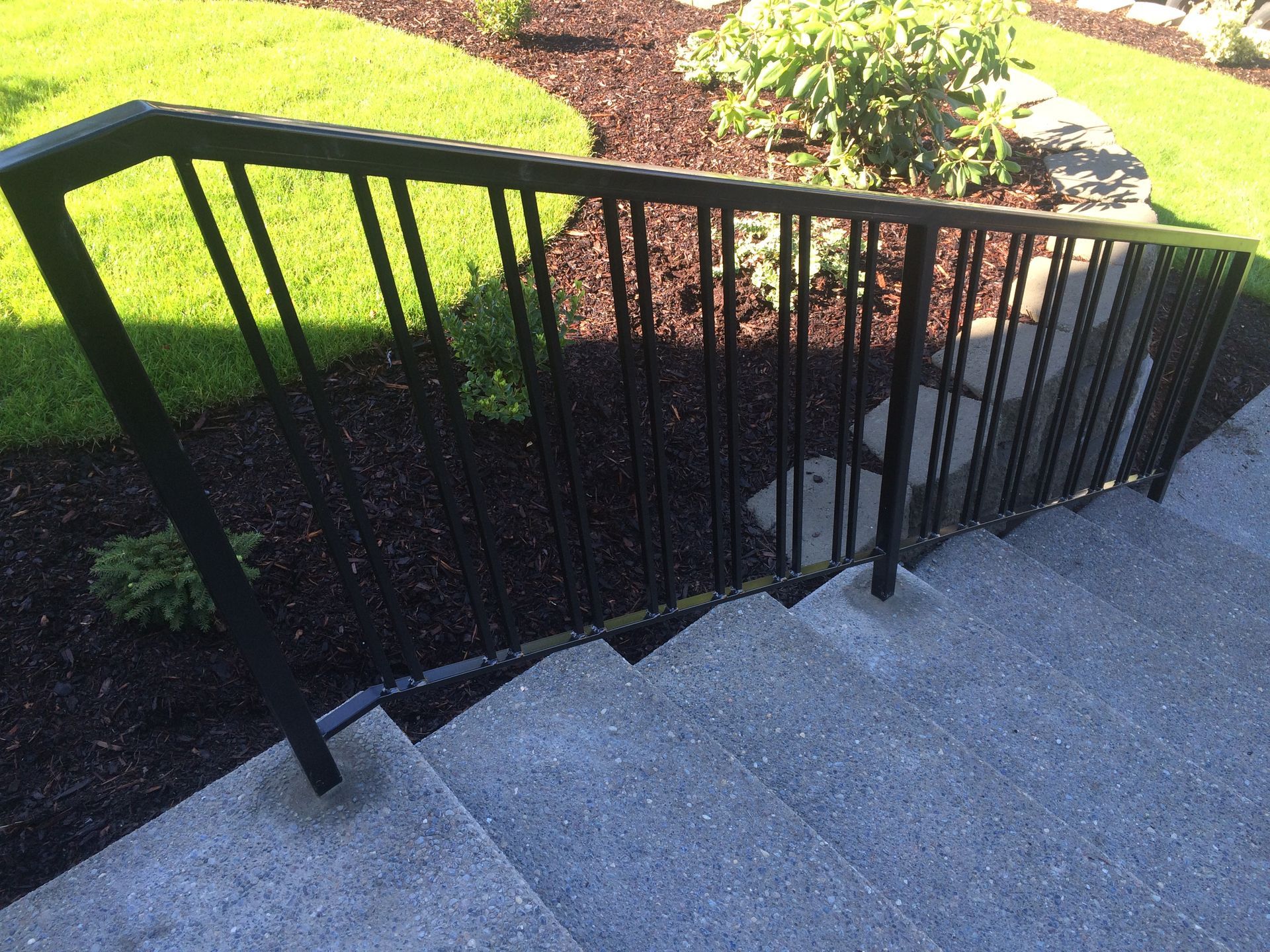 A black railing on a set of stairs with a garden in the background