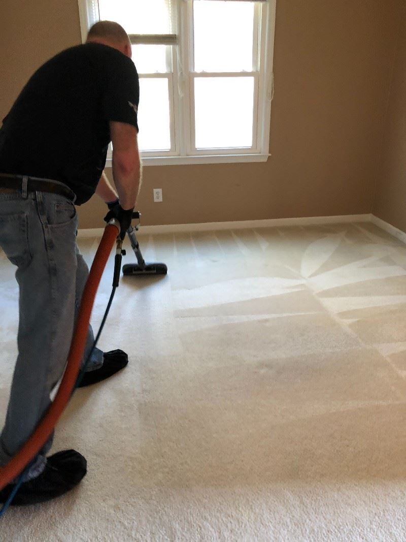 A man is cleaning a carpet with a vacuum cleaner