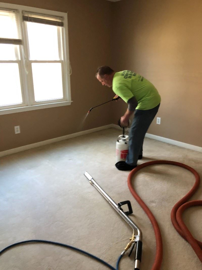 A man in a green shirt is cleaning a carpet with a vacuum cleaner.