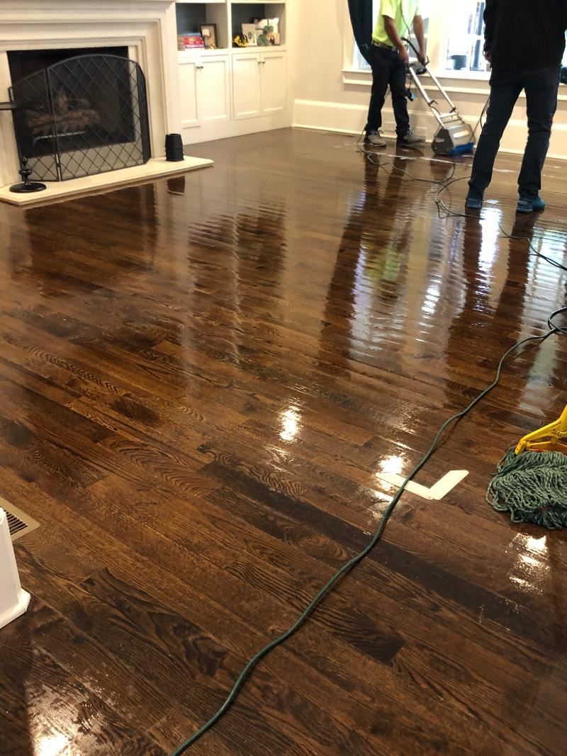 A group of people are cleaning a wooden floor in a living room.