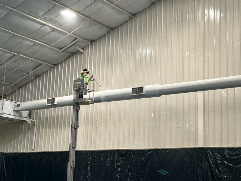 A man is working on a pipe in a warehouse.