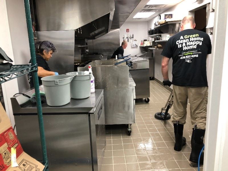 A man wearing a black shirt that says `` a green clean home is a happy home '' is cleaning a kitchen.