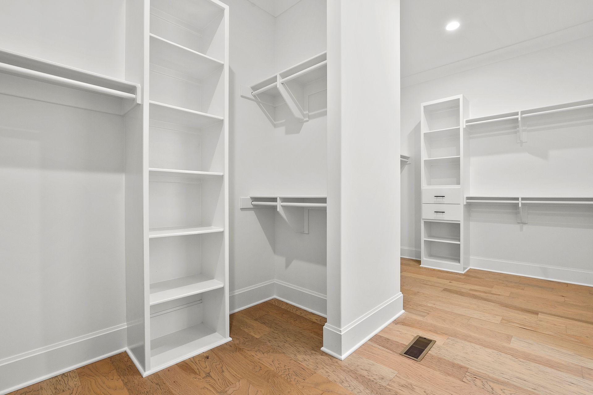 An empty walk in closet with white shelves and wooden floors.