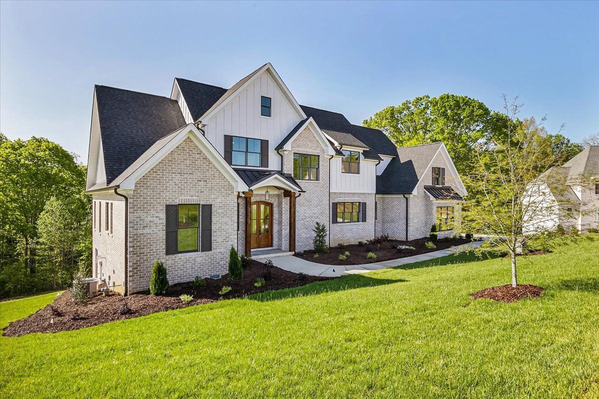 A large white house with a black roof is sitting on top of a lush green hill.