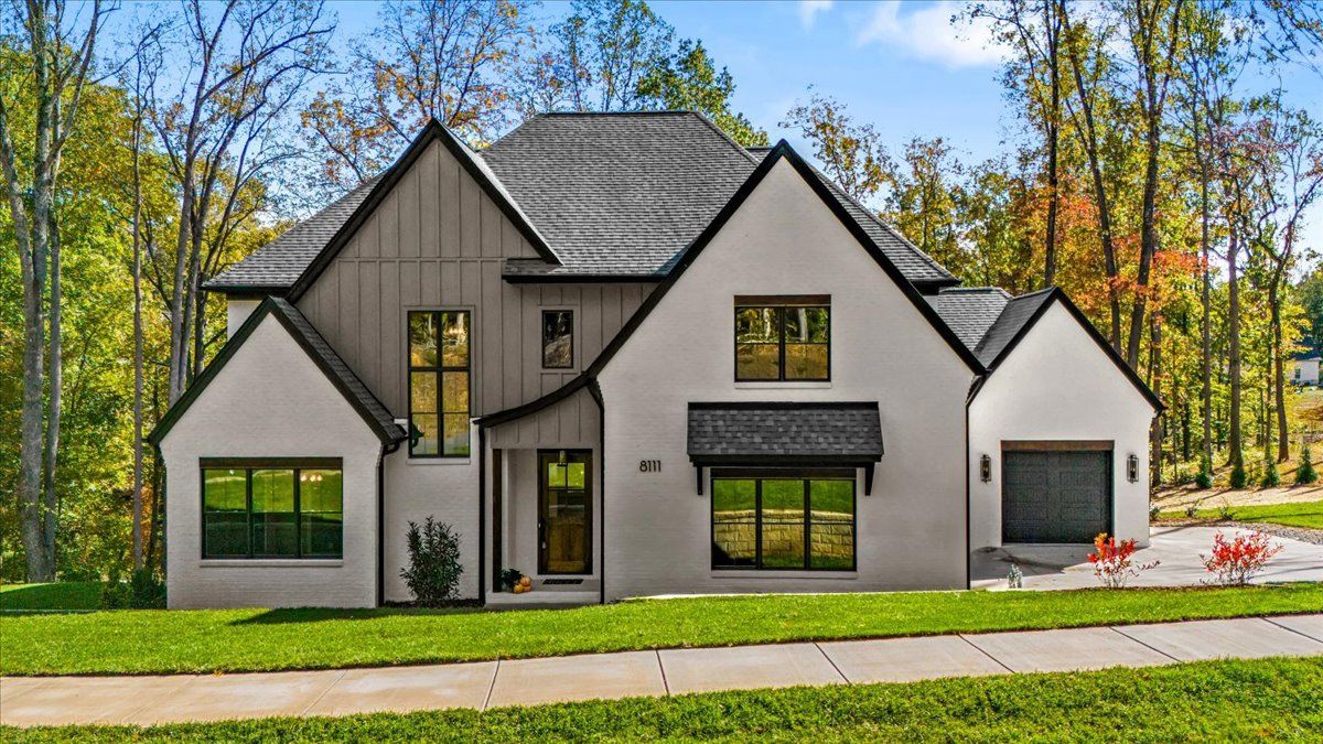 Modern two-story house with white stucco walls, gray roof, black window frames, and green lawn.