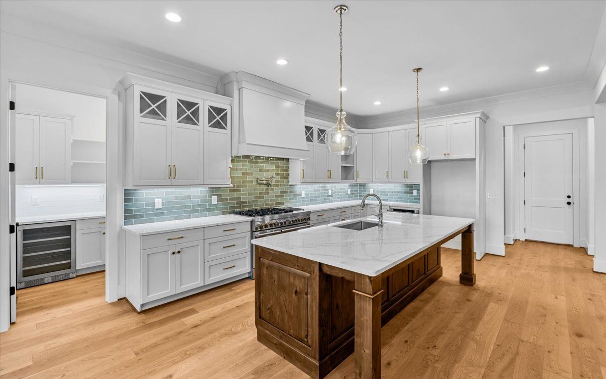 Upscale white kitchen with wood island, marble countertop, and wood flooring.