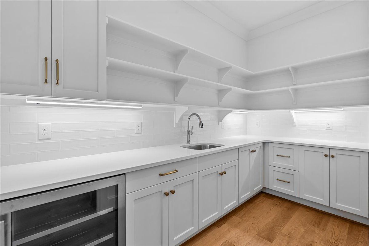 White, bright kitchen with cabinets, shelves, and sink. Wooden floor, countertops, and under-cabinet lighting.