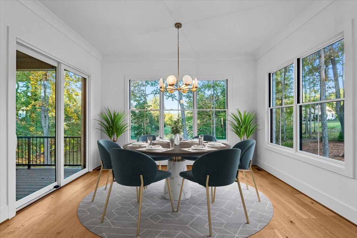 Dining room with round table, blue chairs, gold chandelier, and windows overlooking a green landscape.