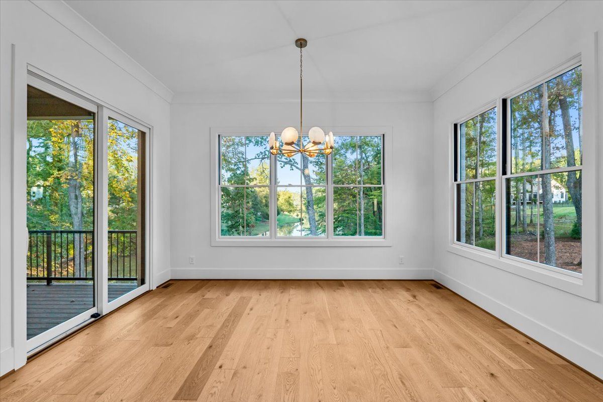 Empty dining room with wood floor, white walls, and large windows overlooking trees.