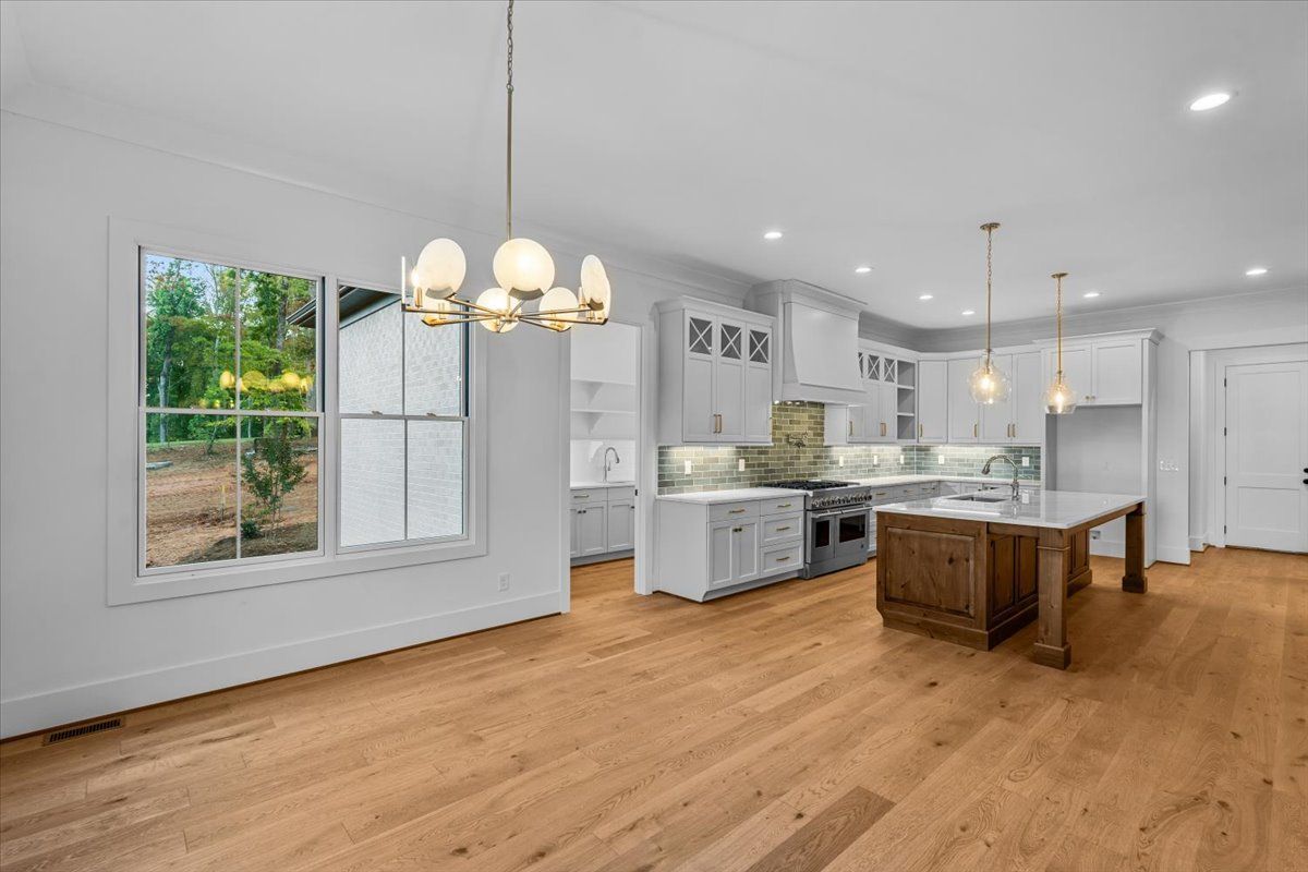 Bright kitchen with hardwood floors, white cabinets, island with marble top, and chandelier.