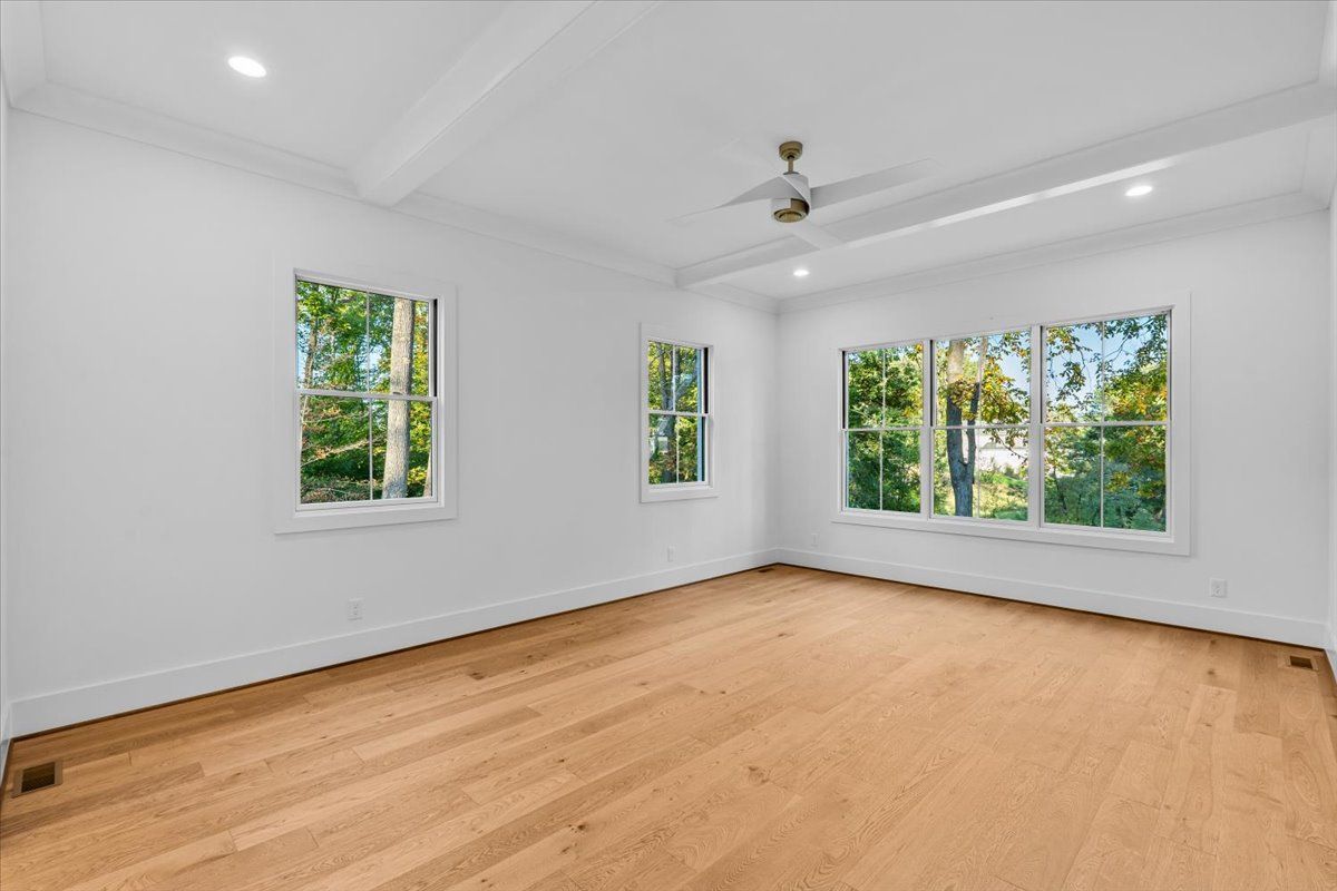 Empty bedroom with hardwood floors, white walls, large windows, and ceiling fan.