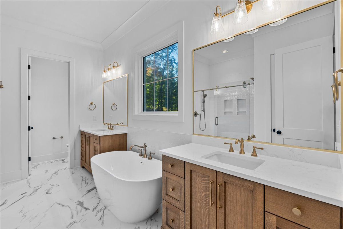Luxurious white marble bathroom with a freestanding tub, wood vanities, and gold fixtures.