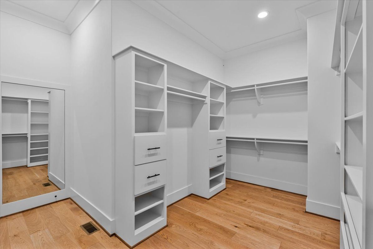 Empty, white walk-in closet with built-in shelves, drawers, and hanging rods. Light wood floor.
