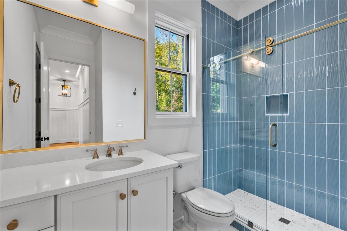 Bathroom with blue tiled shower, white vanity, and gold accents.