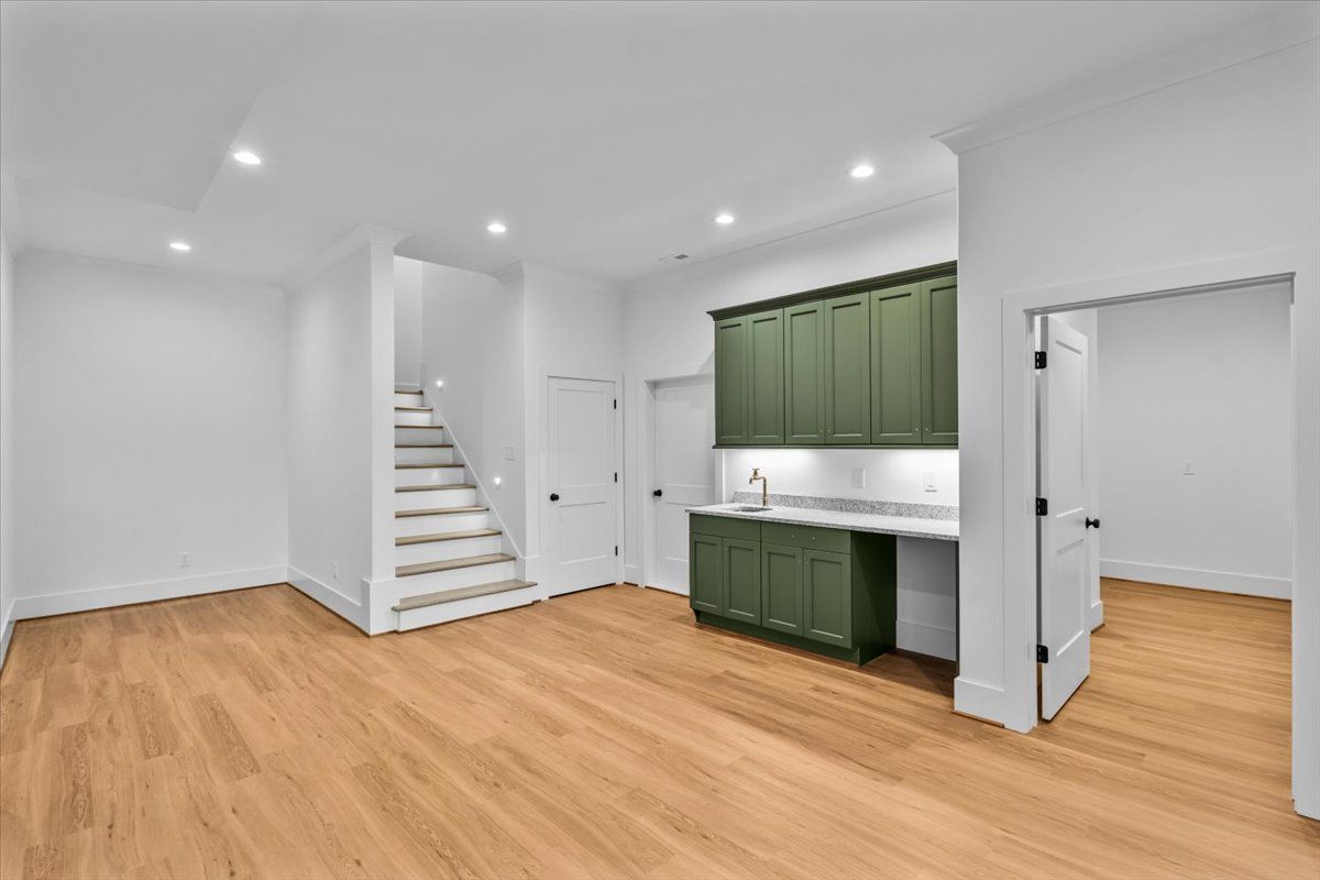 Empty room with hardwood floors, stairs, green cabinets, and white walls.