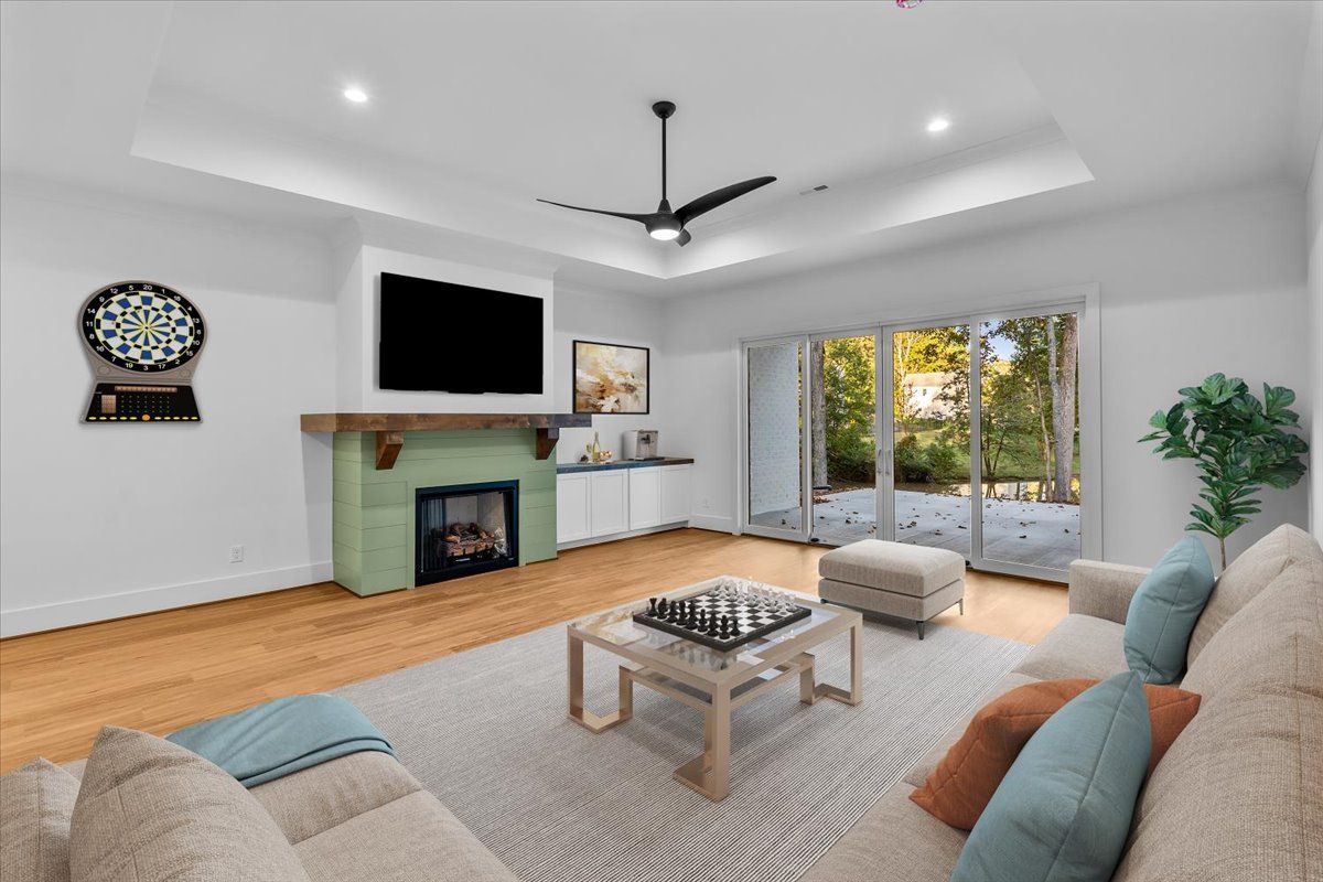 Living room with fireplace, TV, and sliding glass doors to a wooded area. Light-colored walls and wood flooring.