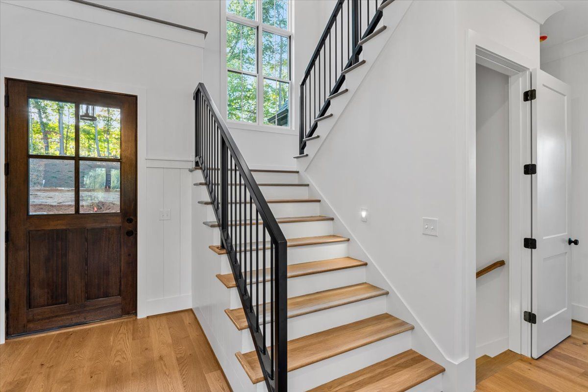 Interior hallway with stairs, dark wood door, and white walls. Light wood flooring and steps. Black railing.
