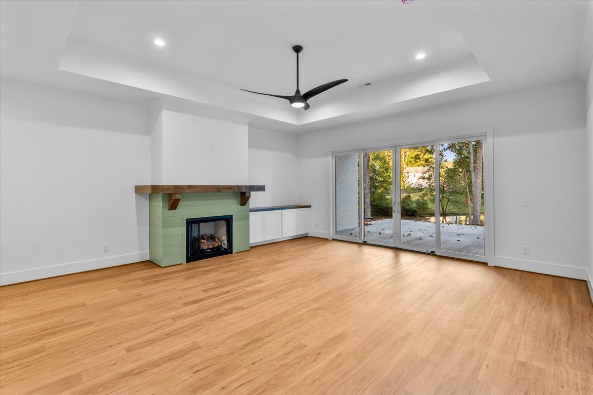 Empty living room with fireplace, hardwood floors, and sliding glass doors to a backyard view.