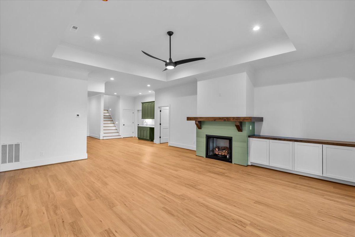 Spacious, light-filled living area with hardwood floors, fireplace, and built-in cabinets. Green accents and a ceiling fan.
