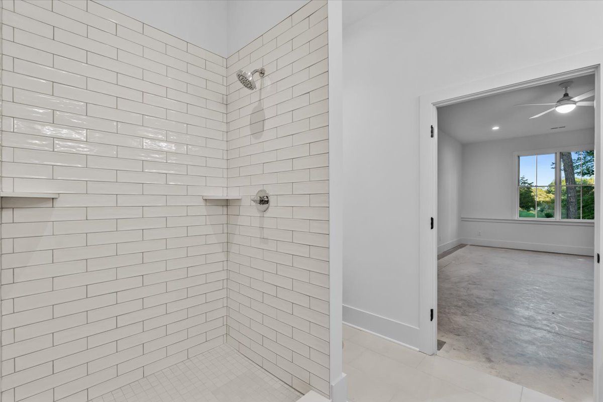 White-tiled shower with built-in shelves. Open door leads to a light-filled room with a window.