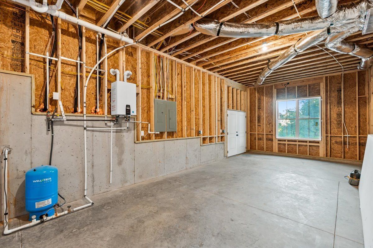 Unfinished room with exposed wooden studs, concrete floor, water tank, and a window with natural light.