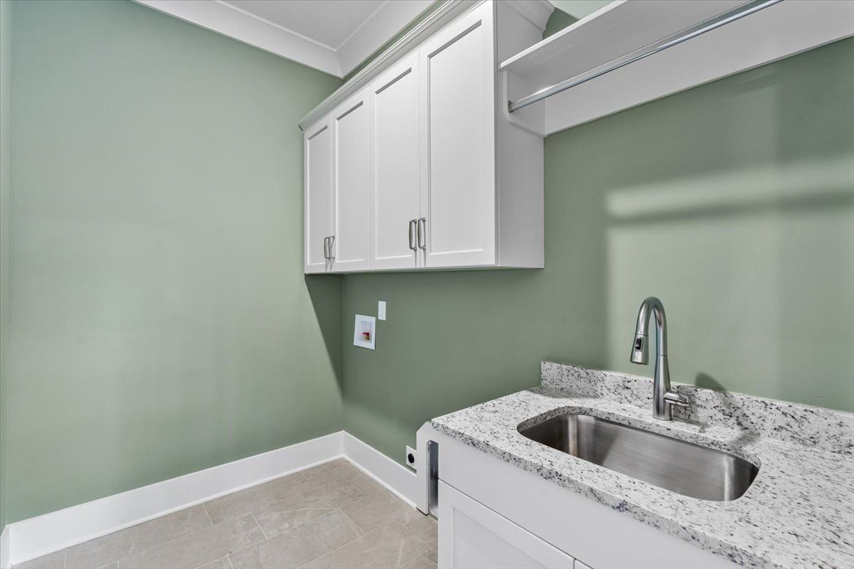 Laundry room with white cabinets, green walls, stainless steel sink, and granite countertop.