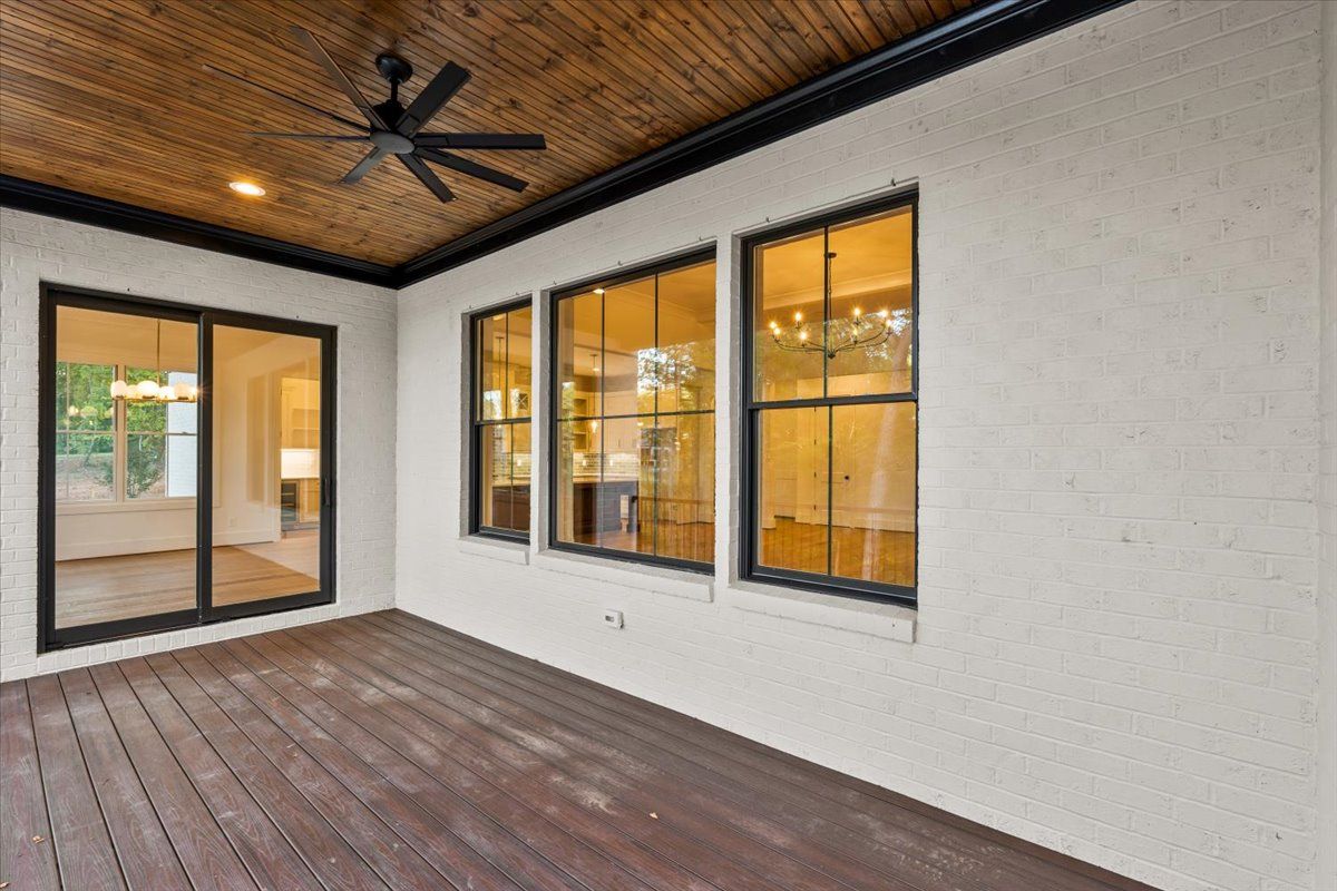 Covered patio with dark wood ceiling, brown deck, white stucco wall, black-framed windows.