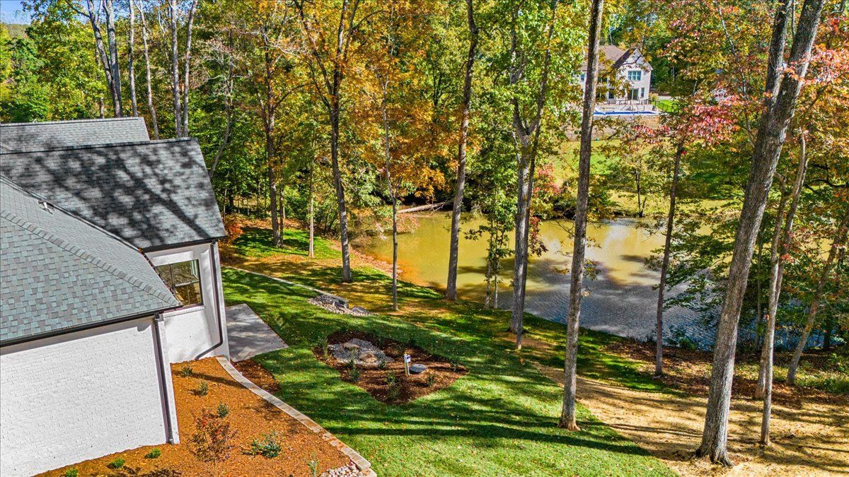 House exterior with trees and water in the background; green grass and autumn foliage.